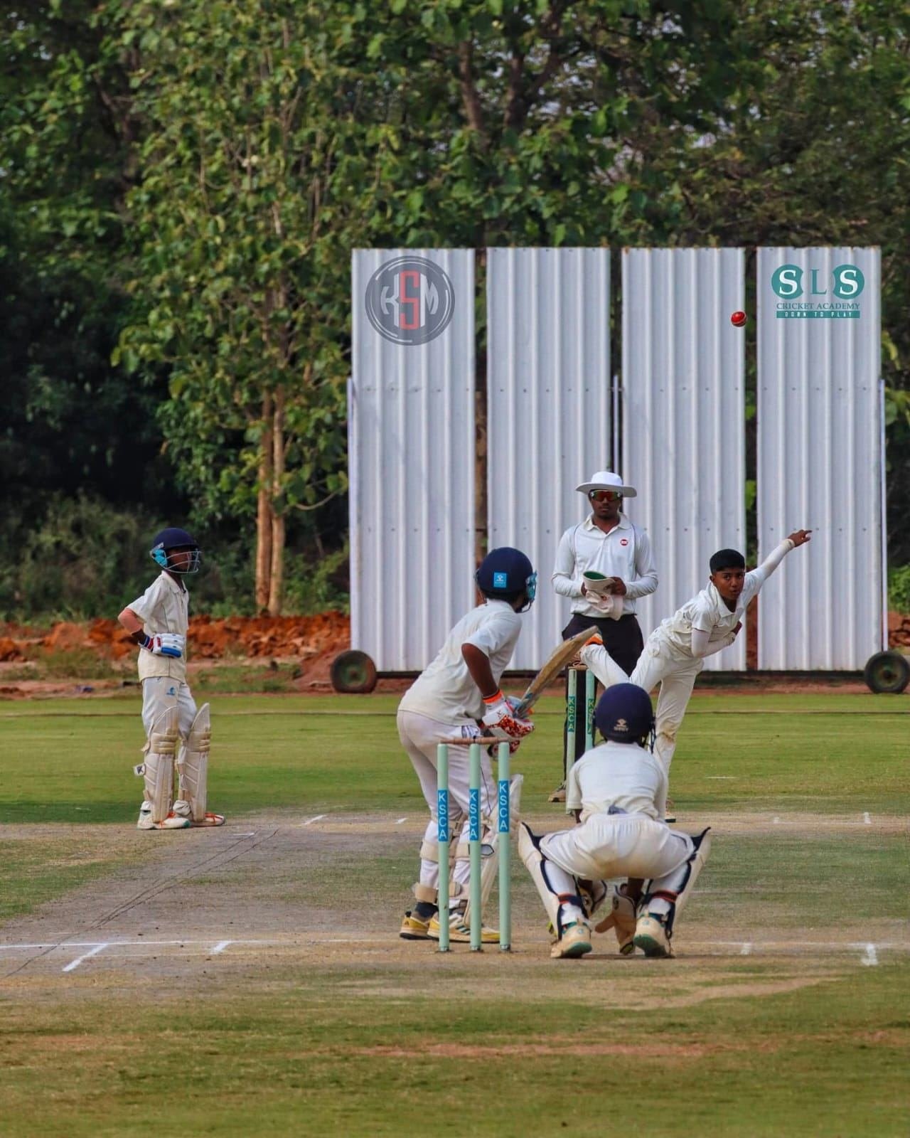 Under-12 cricketers in a match at the KSM U-12 Championship, bowler mid-delivery with fielders in position