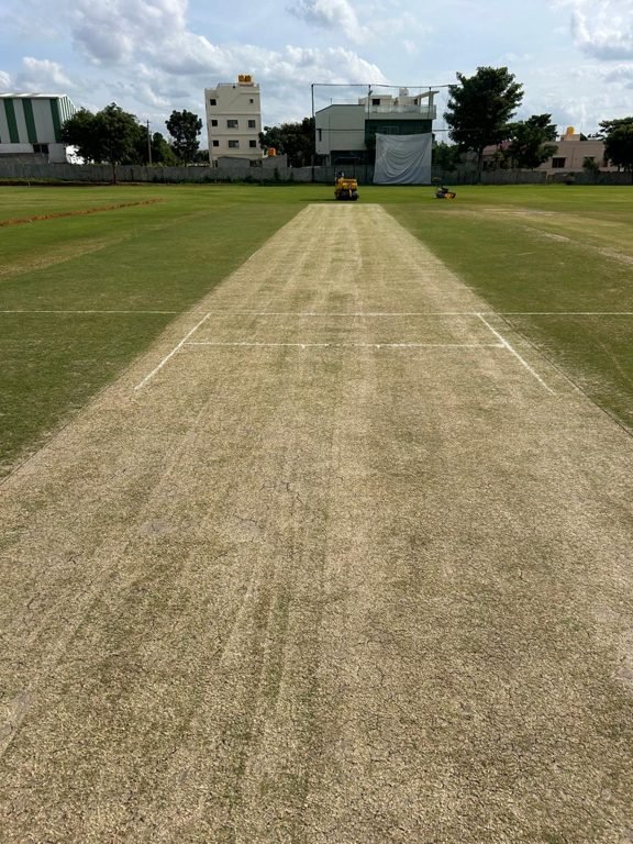 Groundsman mowing the outfield of a natural turf cricket ground at sunrise in Bengaluru