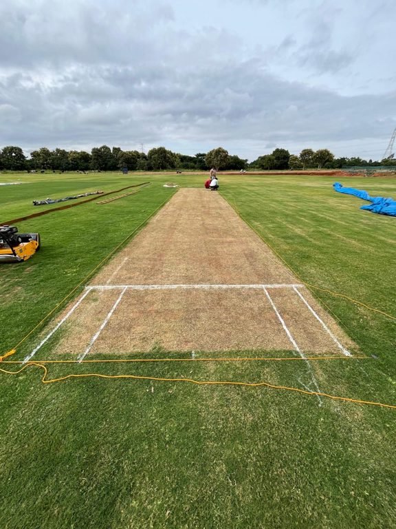 Ground staff preparing a natural turf cricket wicket with a heavy roller at a Kreedangana-built cricket ground